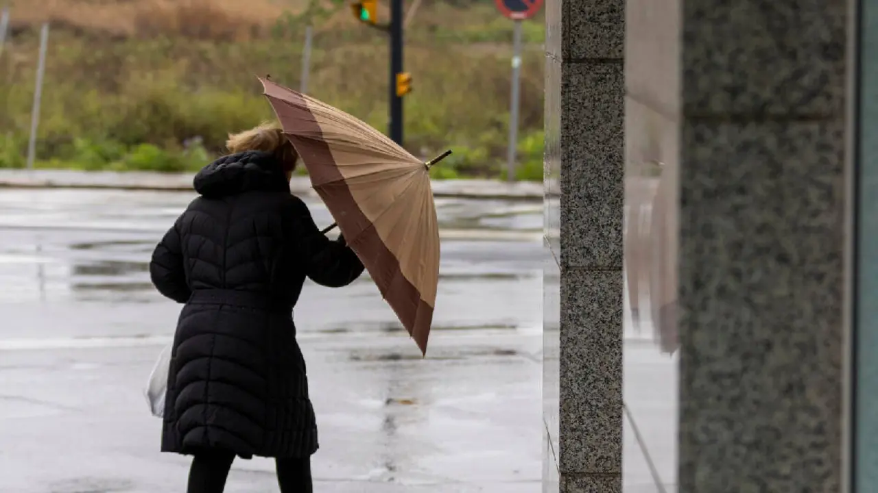 Una mujer se protege de la lluvia y el viento mientras avanza con dificultad por la calle // EMA 112